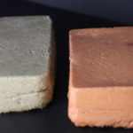 Two blocks of lentil tofu. On the left side is greenisch tofu block made out of brown lentils and on the right side orangisch block of lentil tofu.